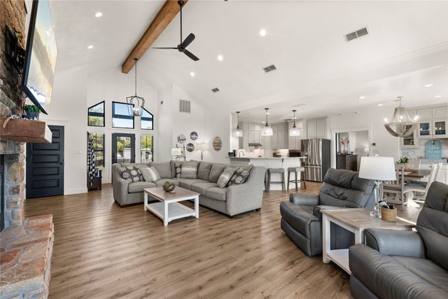 Living room featuring ceiling fan, beamed ceiling, high vaulted ceiling, light wood-style flooring, and a fireplace | Image 15