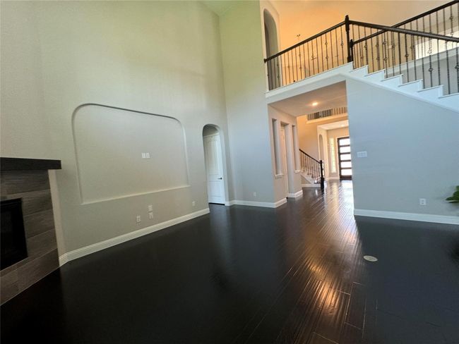 Unfurnished living room with stairs, a tiled fireplace, wood finished floors, arched walkways, and a towering ceiling | Image 21