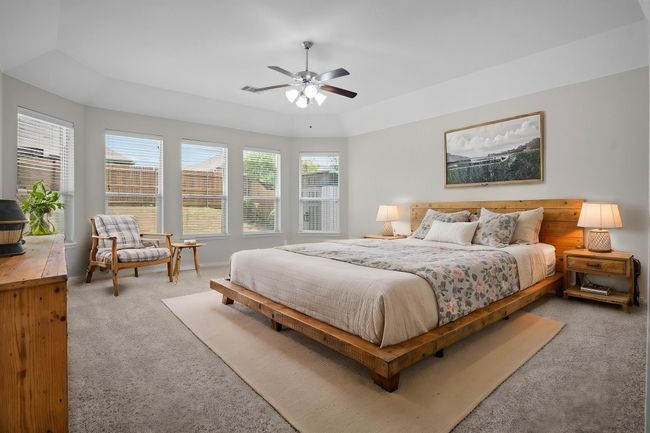 VIRTUALLY STAGED Bedroom featuring a ceiling fan, visible vents, light colored carpet, baseboards, and a tray ceiling | Image 14