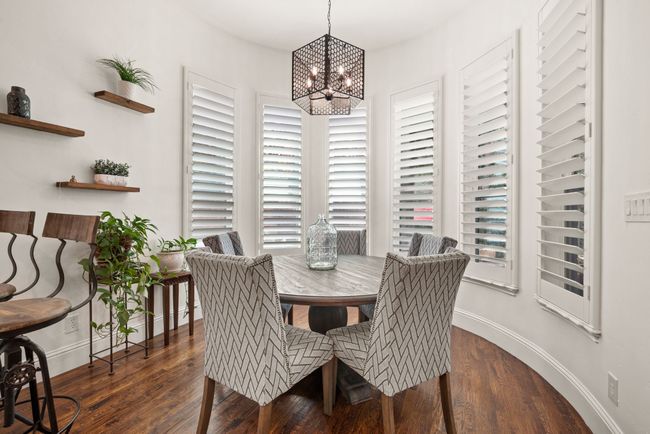 The Breakfast Room features a fashionable chandelier, a bay window with wood shutters, and wood floors | Image 10