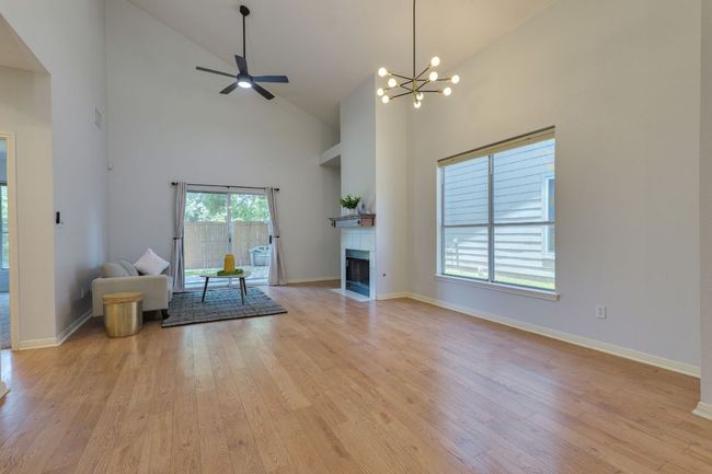 Unfurnished living room with high vaulted ceiling, light wood-type flooring, a tile fireplace, ceiling fan, and a chandelier | Image 12