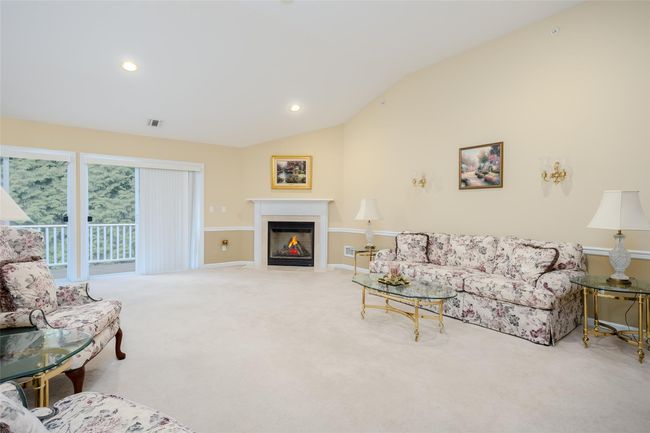 Carpeted living area featuring vaulted ceiling, a fireplace with flush hearth, and recessed lighting | Image 9