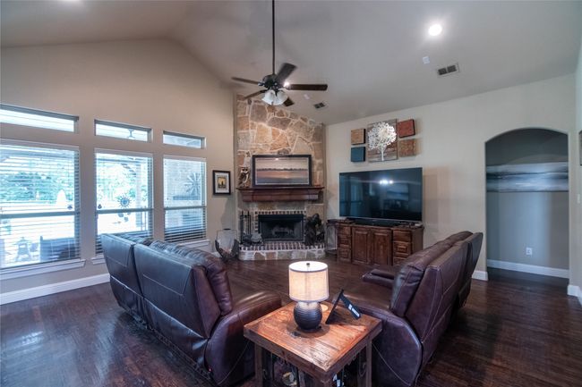 Living room with arched walkways, a ceiling fan, a fireplace, wood finished floors, and high vaulted ceiling | Image 10