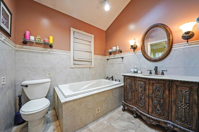 Bathroom featuring tile walls, vanity, lofted ceiling, toilet, and a garden tub | Image 16