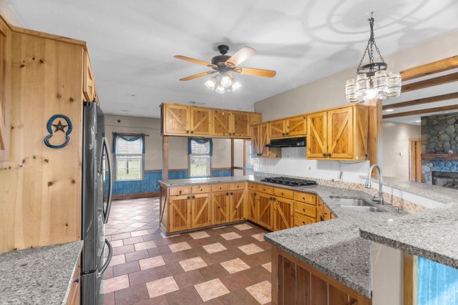 Kitchen with ceiling fan with notable chandelier, a peninsula, under cabinet range hood, a sink, and stainless steel appliances | Image 17