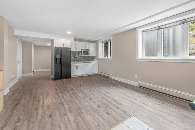 Kitchen with black refrigerator with ice dispenser, a baseboard radiator, stainless steel microwave, white cabinetry, and baseboards | Image 29
