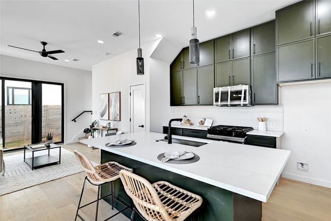 Kitchen with black gas range oven, sink, hanging light fixtures, a breakfast bar, and green cabinets | Image 9