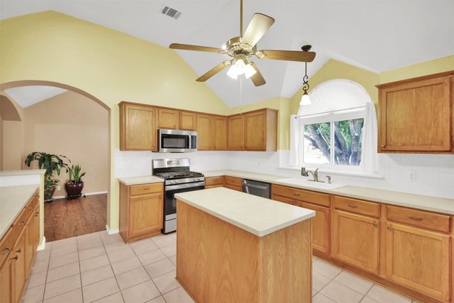 Kitchen featuring appliances with stainless steel finishes, vaulted ceiling, ceiling fan, light countertops, and a kitchen island | Image 16