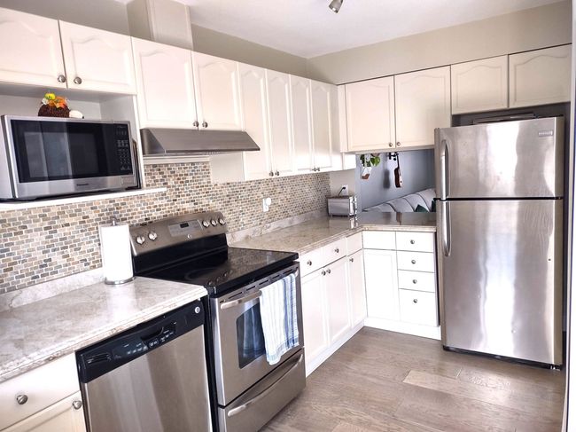 Kitchen with tasteful backsplash, light wood-style flooring, white cabinets, under cabinet range hood, and stainless steel appliances | Image 7