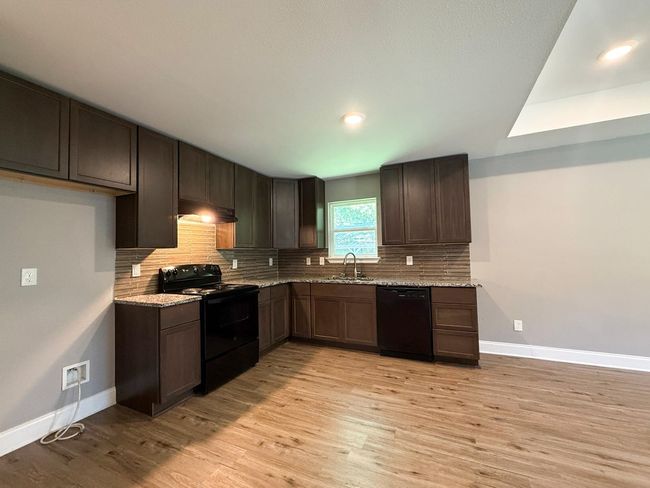 Kitchen featuring black appliances, decorative backsplash, light wood-type flooring, light stone counters, and dark brown cabinetry | Image 5