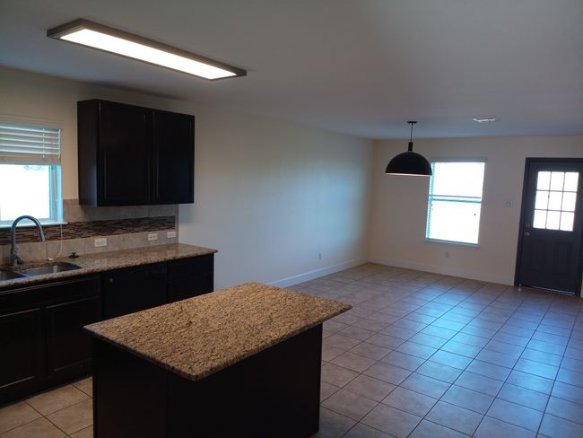 Kitchen with dark cabinets, light tile patterned flooring, light stone counters, and decorative backsplash | Image 6