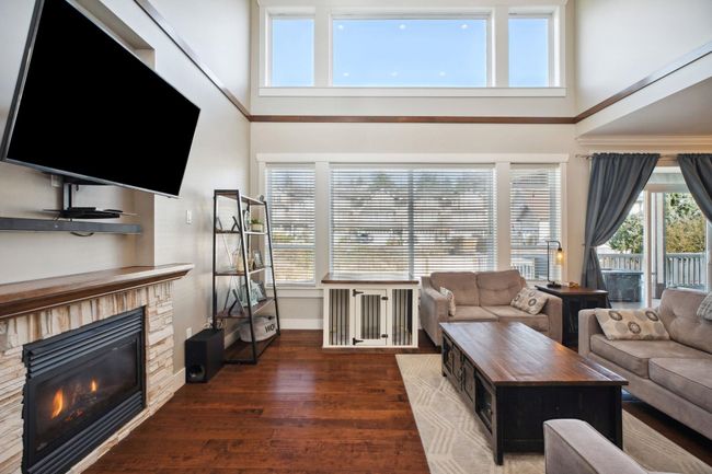 Living room with a towering ceiling, a stone fireplace, baseboards, and wood finished floors | Image 4