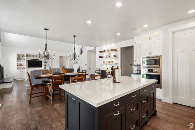 Kitchen featuring white cabinets, open floor plan, appliances with stainless steel finishes, a chandelier, and dark wood finished floors | Image 12