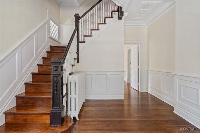 Stairs featuring a decorative wall, crown molding, wainscoting, wood finished floors, and radiator | Image 24