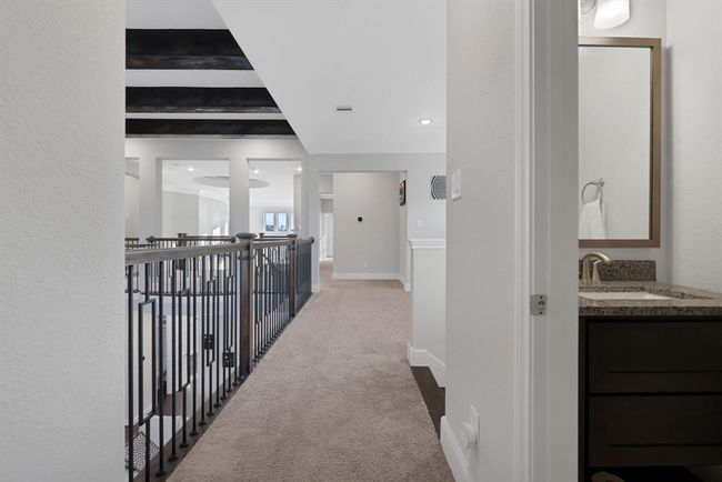 The upper-level hallway with carpeted flooring, featuring an open railing that overlooks the level below. | Image 39