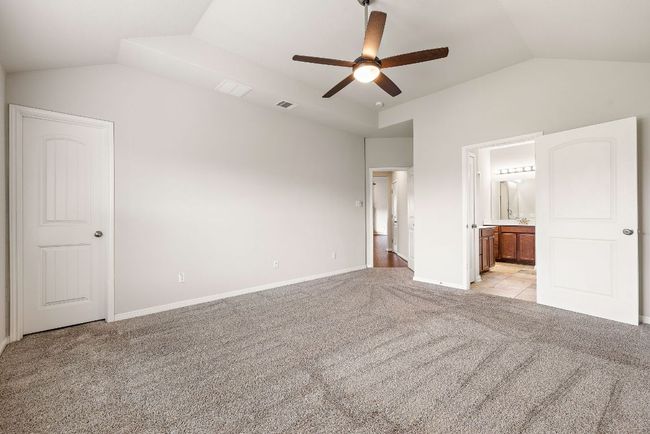 Unfurnished bedroom featuring lofted ceiling, visible vents, connected bathroom, baseboards, and light colored carpet | Image 17
