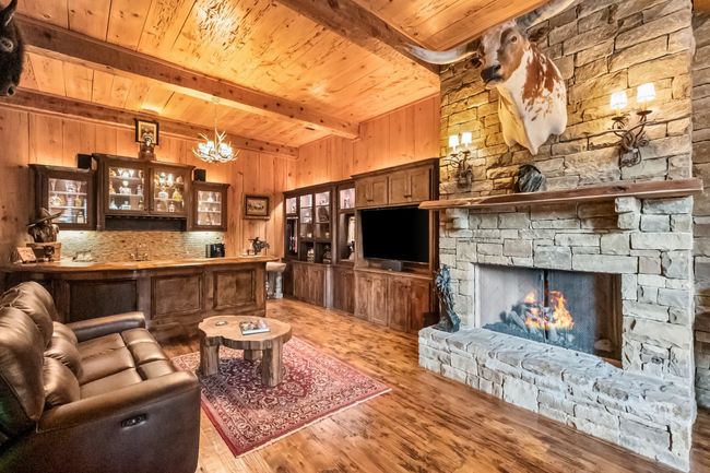 Living room with pecky cypress ceiling, walls, exposed beams, wood floors, a chandelier, and a stone fireplace | Image 17