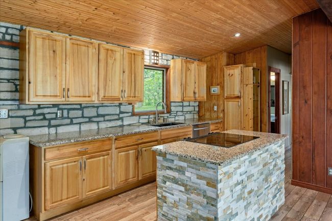 Kitchen with wood ceiling, light wood-type flooring, backsplash, cooktop, and a kitchen island | Image 11