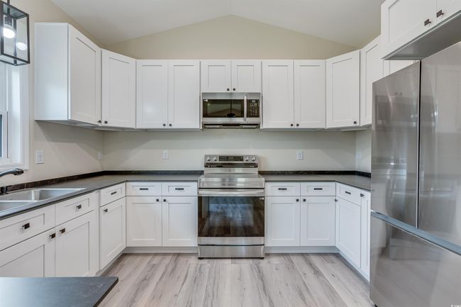 Kitchen featuring appliances with stainless steel finishes, a sink, lofted ceiling, dark countertops, and white cabinetry | Image 9
