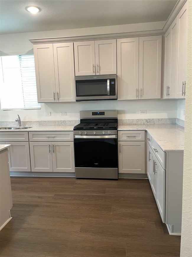Kitchen with stainless steel gas range oven, a sink, dark wood finished floors, and recessed lighting | Image 5