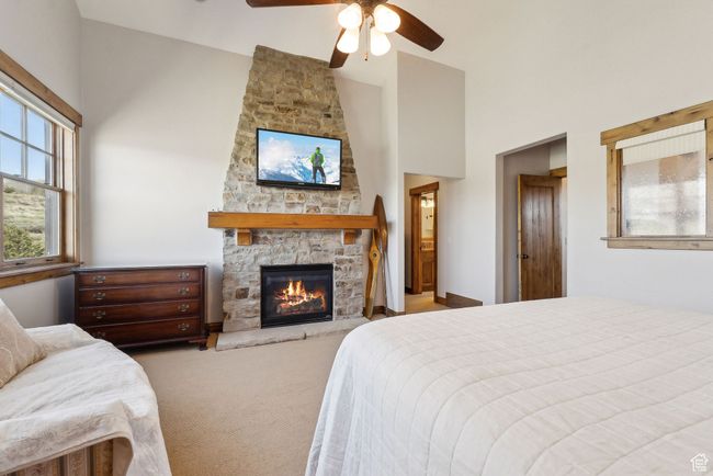 Carpeted bedroom with a stone fireplace, a ceiling fan, and high vaulted ceiling | Image 16