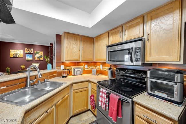 Kitchen with stainless steel microwave, light countertops, a sink, and black range with electric cooktop | Image 10