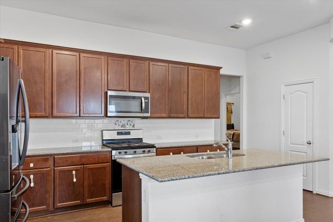 Kitchen with light stone counters, visible vents, a sink, tasteful backsplash, and appliances with stainless steel finishes | Image 12