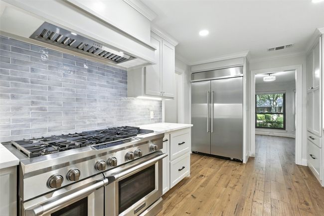 Kitchen featuring high quality appliances, custom range hood, tasteful backsplash, light wood-type flooring, and white cabinetry | Image 13