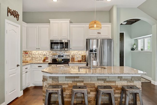 Kitchen featuring stainless steel appliances, arched walkways, light stone countertops, decorative backsplash, and a breakfast bar | Image 13