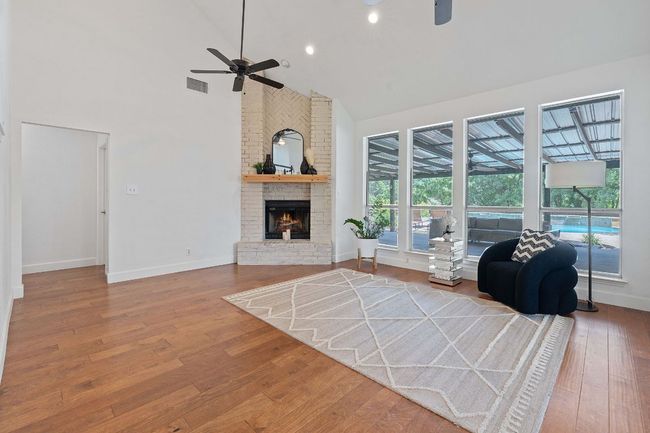 Living area featuring ceiling fan, high vaulted ceiling, wood finished floors, a fireplace, and a sunroom | Image 13