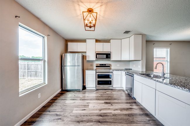 Kitchen with appliances with stainless steel finishes, a sink, light stone countertops, white cabinets, and light wood-style floors | Image 10