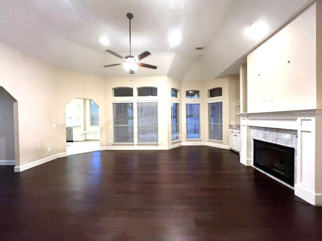 Unfurnished living room with a ceiling fan, dark wood-style flooring, a fireplace, arched walkways, and a towering ceiling | Image 22