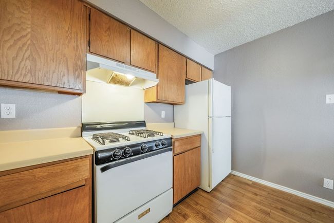 Kitchen featuring white appliances, under cabinet range hood, light wood-type flooring, light countertops, and a textured ceiling | Image 17