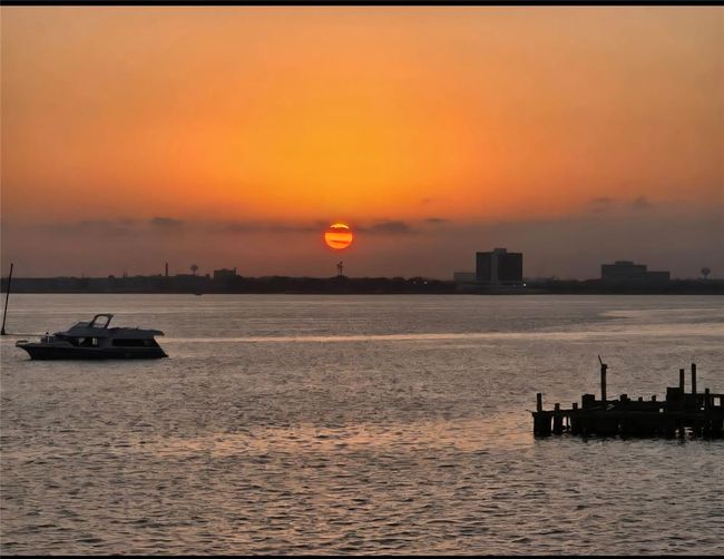 This photo features a serene waterfront view at sunset, with a boat on the water and a wooden dock in the foreground. The skyline is silhouetted against the vibrant orange sky, creating a peaceful and picturesque setting. Ideal for buyers seeking a tranquil coastal lifestyle. | Image 17