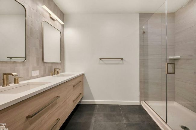 Bathroom featuring double vanity, tile patterned floors, a shower stall, and baseboards | Image 5