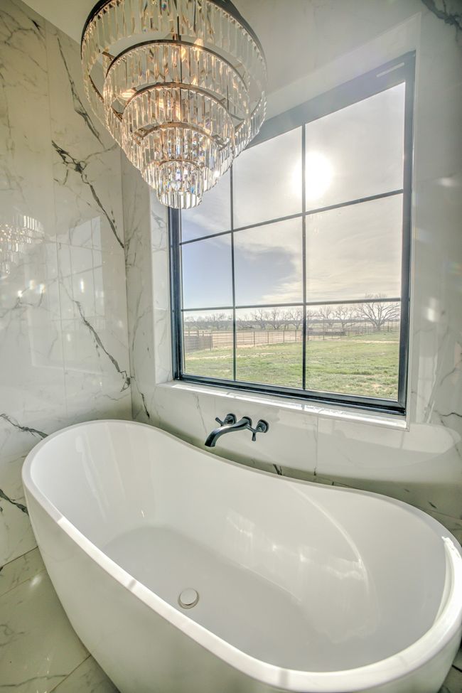 Full bathroom featuring a healthy amount of sunlight, stone wall, a freestanding bath, and marble finish floor | Image 14