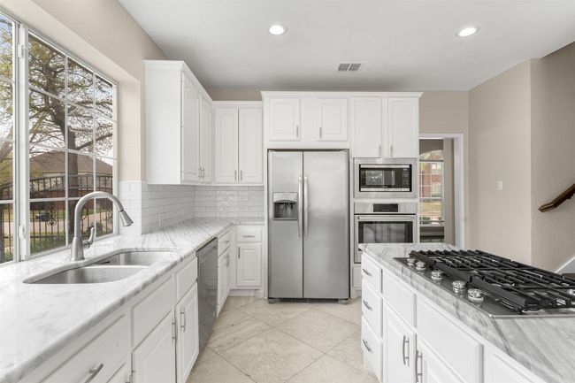 Kitchen with a sink, appliances with stainless steel finishes, visible vents, white cabinets, and decorative backsplash | Image 12
