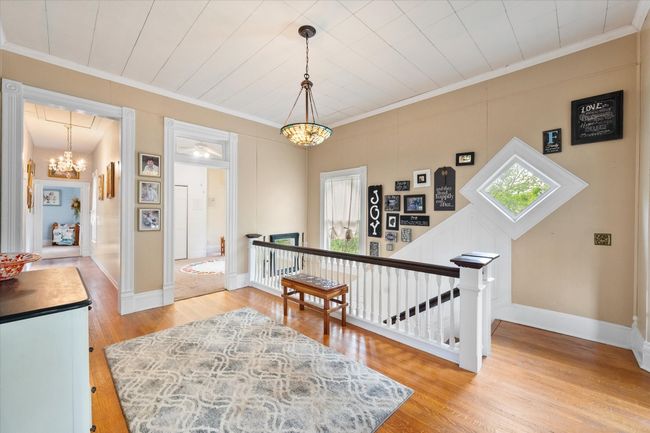 Hall with a chandelier, an upstairs landing, crown molding, wood finished floors, and baseboards | Image 21