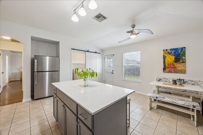 Kitchen featuring freestanding refrigerator, a barn door, ceiling fan, light tile floors, and a kitchen island | Image 10
