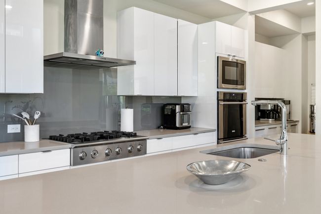 Kitchen with wall chimney exhaust hood, stainless steel appliances, modern cabinets, light countertops, and white cabinets | Image 20