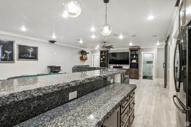 Kitchen featuring freestanding refrigerator, open floor plan, crown molding, hanging light fixtures, and dark stone countertops | Image 70