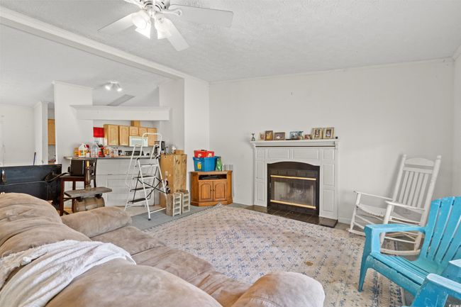 Living area featuring ceiling fan, a fireplace with flush hearth, ornamental molding, and a textured ceiling | Image 18