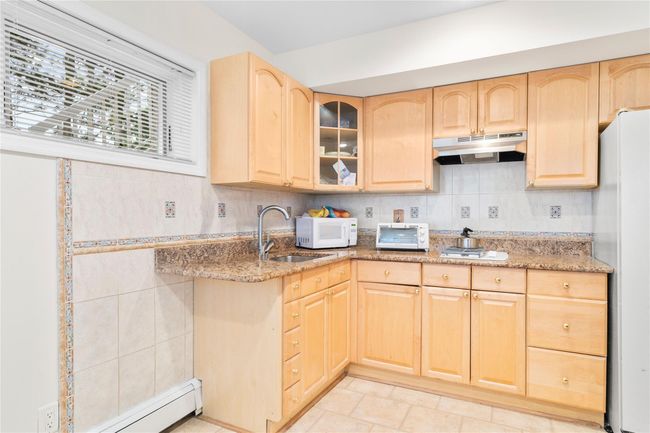 Kitchen featuring light brown cabinetry, white appliances, a sink, under cabinet range hood, and light stone counters | Image 42