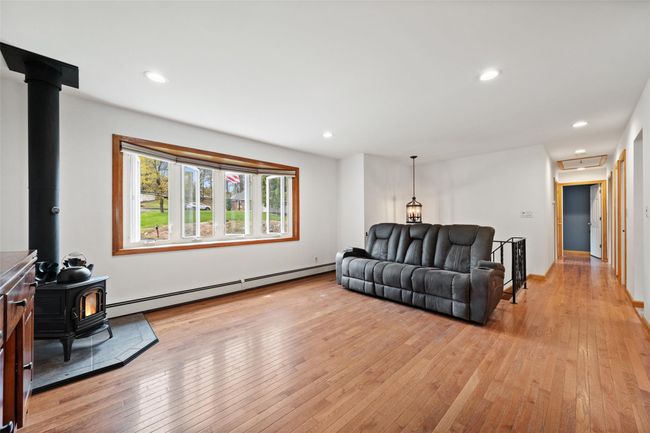 Living area featuring light wood-type flooring, a wood stove, recessed lighting, and a baseboard radiator | Image 4