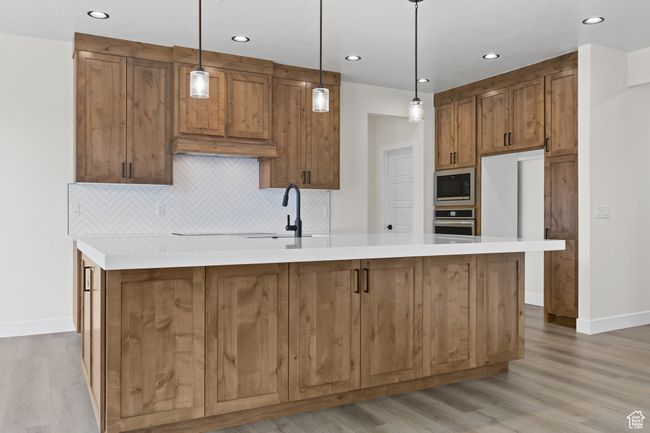 Kitchen featuring a sink, tasteful backsplash, a center island with sink, brown cabinets, and stainless steel appliances | Image 5