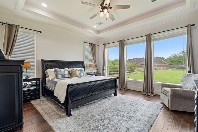 Serenity can be found in this impressive Primary Suite. Five large windows welcome in the desirable natural light, while also providing a calming pastoral view of the Back and Side Yards. Warm and rich wood floor dresses up the space, making the white baseboards and crown molding pop. | Image 26