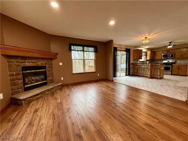 Unfurnished living room featuring light wood finished floors, a stone fireplace, a sink, baseboards, and recessed lighting | Image 11