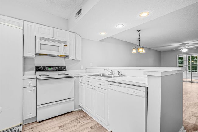 Kitchen with white appliances, a textured ceiling, a peninsula, light wood finished floors, and light countertops | Image 7