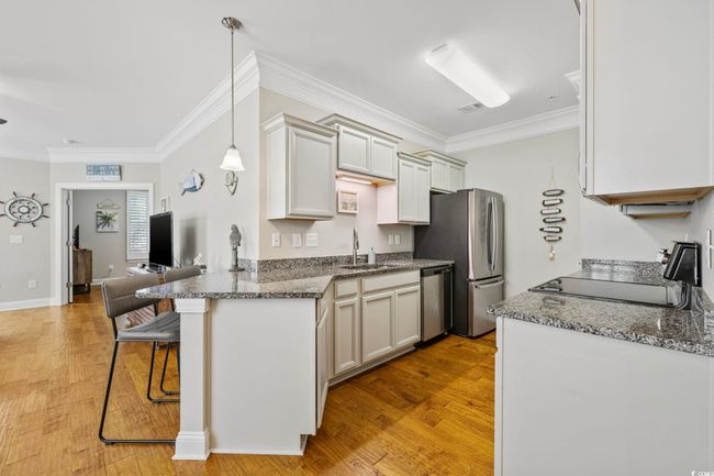 Kitchen with appliances with stainless steel finishes, a sink, a breakfast bar area, ornamental molding, and light wood-style floors | Image 11