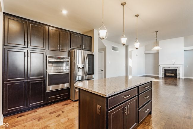 kitchen featuring stainless steel appliances, visible vents, light wood-style floors, light stone countertops, and dark brown cabinetry | Image 22